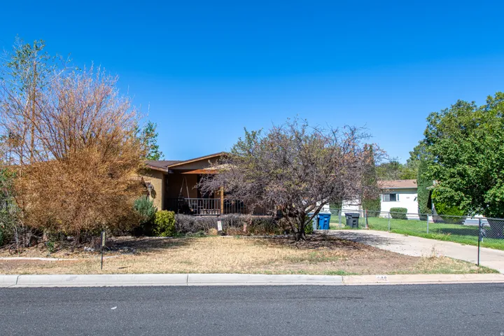 Property exterior featuring a covered porch with railing, sloped roofline, and established trees