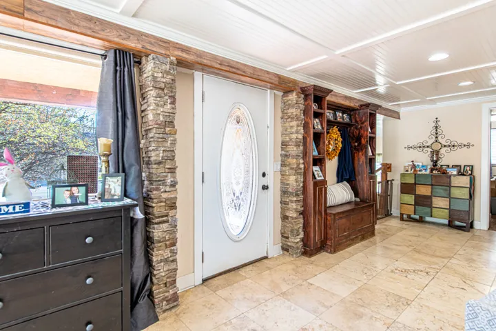 Entryway featuring stone veneer accents, an oval decorative glass door, a built-in wood-finish hall tree, and large format tile flooring