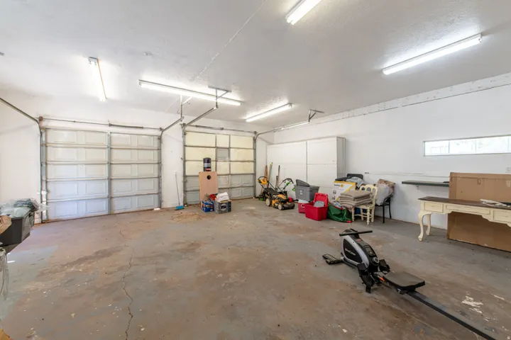 Spacious garage featuring two overhead doors, concrete flooring, overhead fluorescent lighting, and white walls