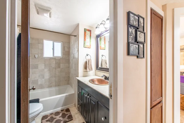 Bathroom featuring a single vanity with a copper-finish sink, dark wood cabinetry, and a tile shower surround