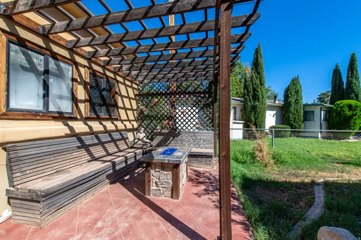 Attached wooden pergola with lattice detailing, built-in wooden bench seating, and an integrated stone-finish table