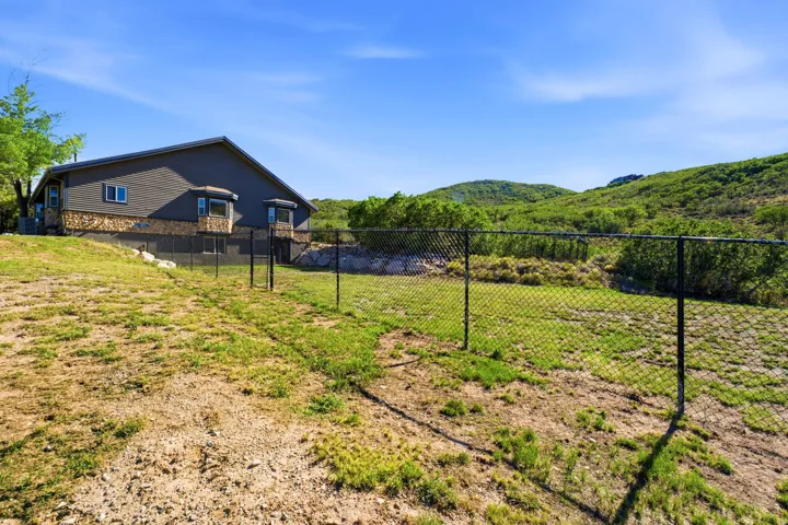 Exterior featuring dark grey siding, stone accents, multiple bay windows, and a black chain-link fence