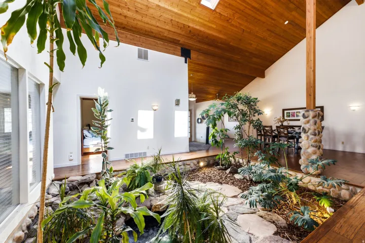 Vaulted wood-paneled ceiling, large skylight, stone-clad interior column, and an indoor garden feature with integrated lighting