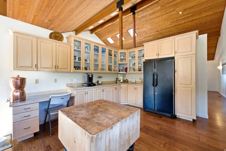 Wood-finish flooring, vaulted wood-plank ceiling, skylights, built-in cabinetry with glass-front uppers, and integrated desk space