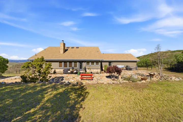 Expansive rear facade featuring a stone chimney, multiple skylights, and a stone-paved patio