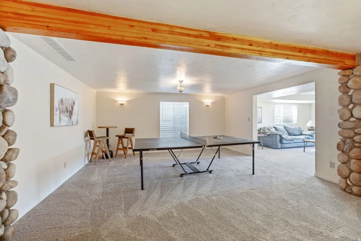 Carpeted recreation area with a wood beam, stone column accents, and wall sconce lighting