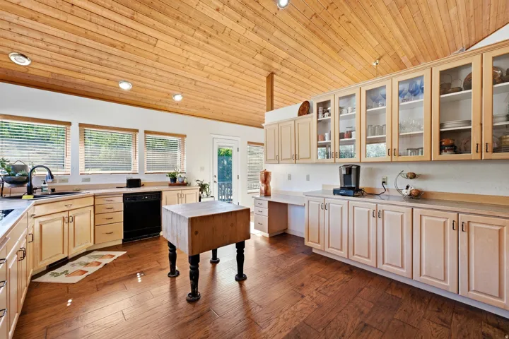 Wood-paneled vaulted ceiling, rich wood-finish flooring, light-toned cabinetry, integrated sink, and multiple windows