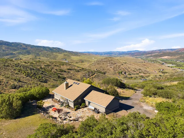 Expansive natural landscape with rolling hills, a brown shingled roof, a stone chimney, and a stone patio area