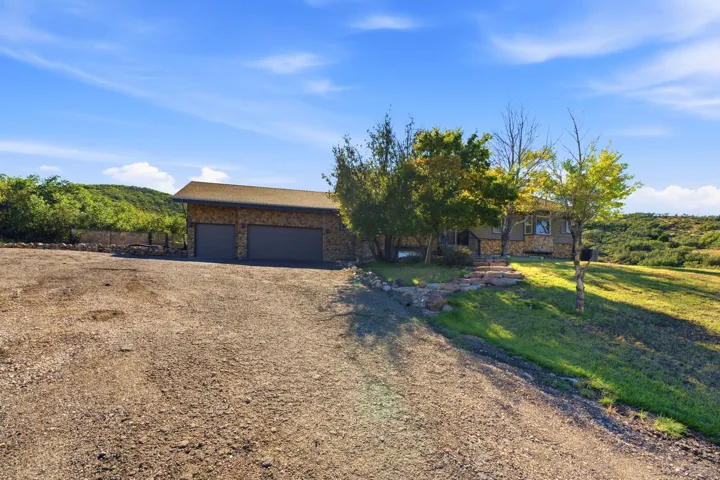 Stone-clad exterior, two-car garage, gravel driveway, natural rock landscaping, and sloped grassy areas