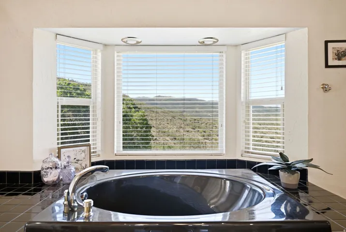Built-in tub with chrome fixtures, set within a bay window featuring horizontal blinds