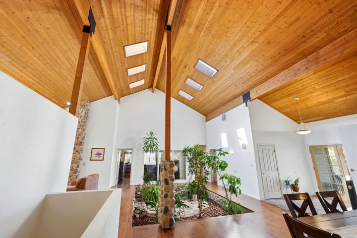 Vaulted wood-paneled ceiling with exposed beams, multiple skylights, hardwood flooring, stone pillar accents, and an interior planter box feature