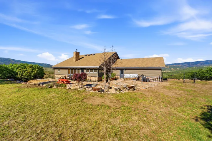 Expansive exterior featuring a stone patio, mature landscaping, and an integrated chimney