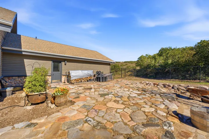 Stone patio with varied natural stone pavers, bordered by a gravel and dirt landscape