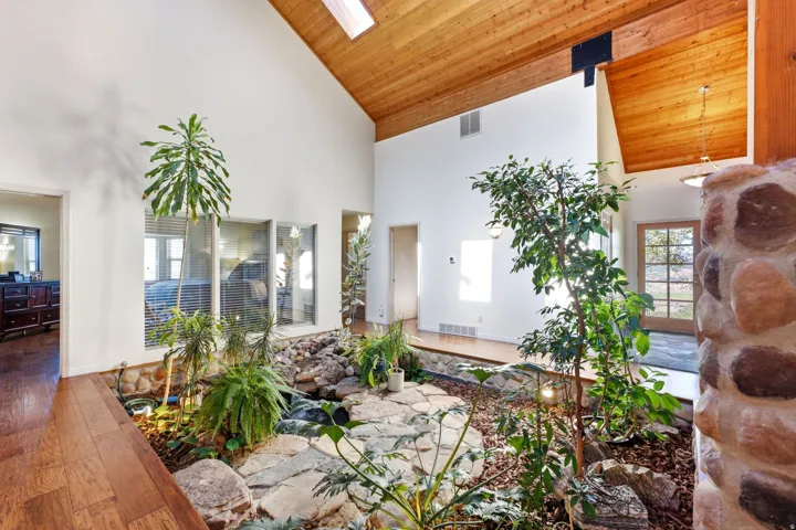 Indoor atrium with natural stone landscaping, wood-finish flooring, vaulted wood-paneled ceiling, and skylight