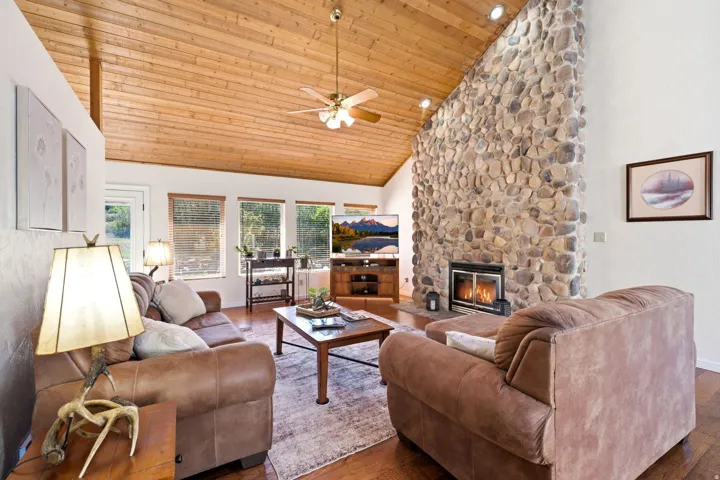 Vaulted wood-plank ceiling, floor-to-ceiling stone fireplace, wood-finish flooring, and multiple windows