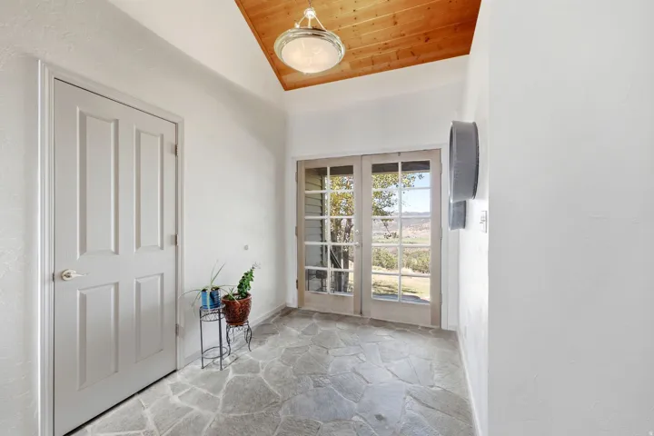 Flagstone flooring, wood-paneled ceiling, glass-paned French doors, and an overhead flush mount light fixture