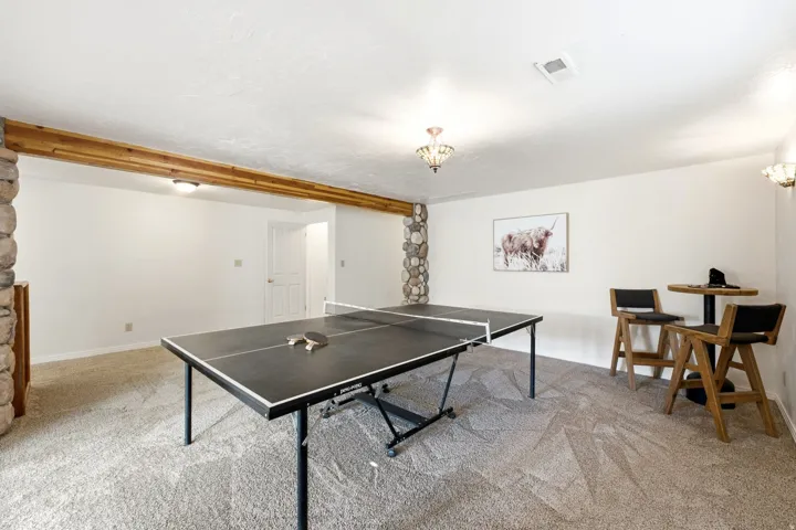 Carpeted room featuring stone-wrapped columns, a wood beam, and flush-mount lighting fixtures