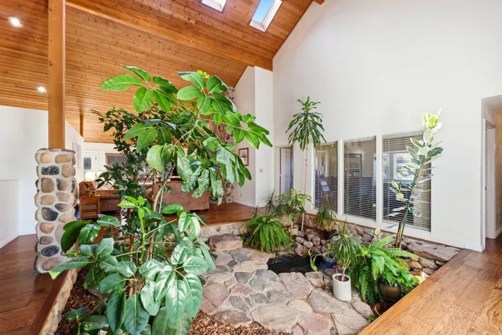 Vaulted wood-paneled ceiling with skylights, interior atrium featuring stone flooring, stone pillar accent, and large interior windows