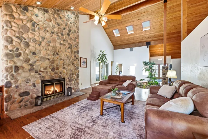 Vaulted wood-paneled ceiling with exposed beams, stone-faced fireplace, skylights, wood-finish flooring, and recessed lighting