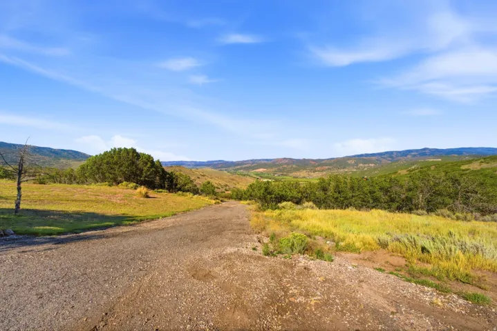 Expansive natural landscape with rolling hills, abundant green foliage, and a clear blue sky overhead