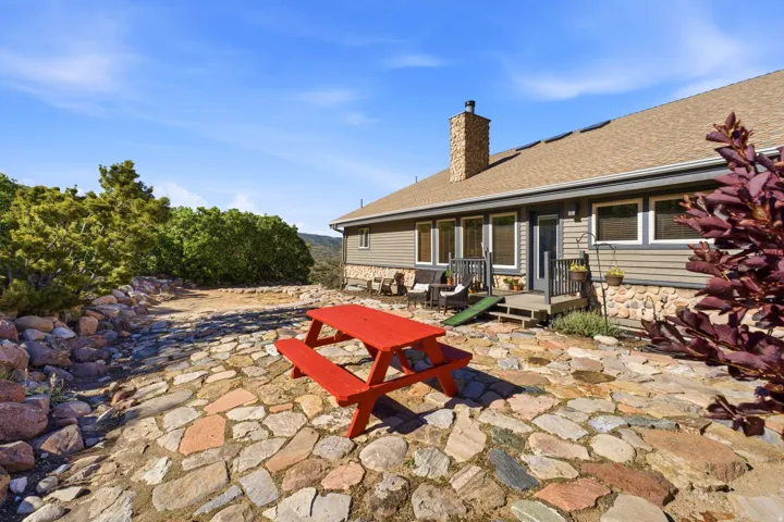 Stone patio with retaining wall, siding exterior, stone chimney, and a composite shingle roof