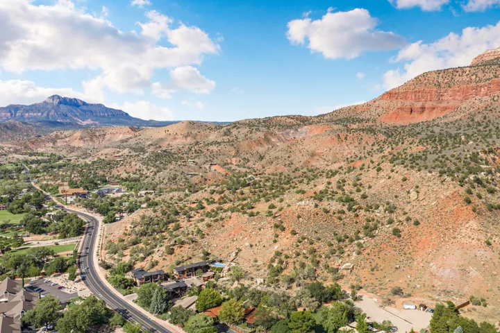 Mountainous landscape with red rock formations and natural vegetation, featuring a winding road and residential structures