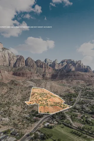 Expansive land parcel featuring natural desert flora, bordering a paved road, with mountainous terrain in the background, set under a blue sky with scattered clouds