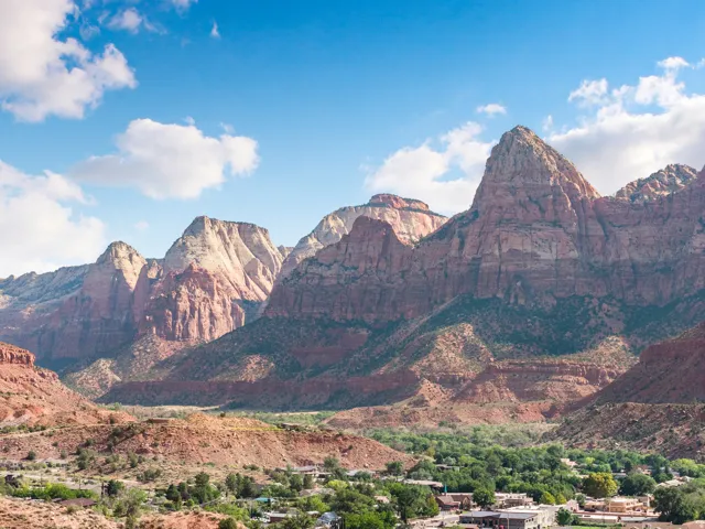 Sweeping desert mountain range, expansive blue sky with scattered clouds, and a distant community nestled within a verdant valley