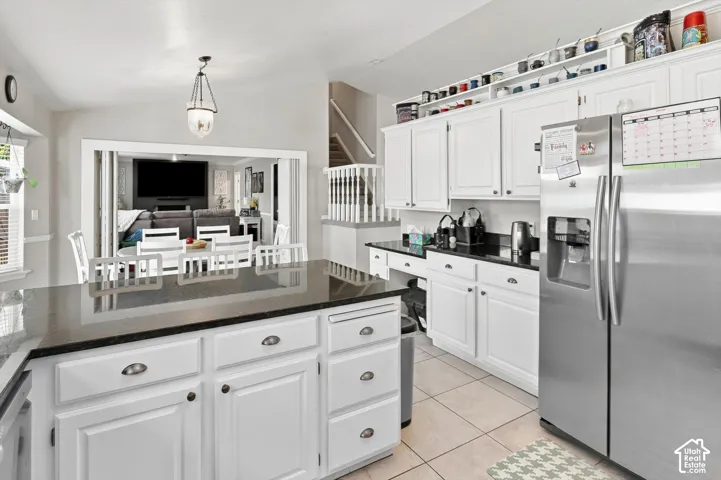 White cabinetry with dark countertops, stainless steel refrigerator, tile flooring, and a kitchen island with storage