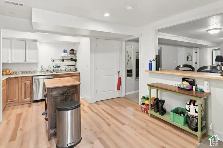 Hardwood-finish flooring throughout, stainless steel dishwasher, white upper cabinetry, wood-finish lower cabinetry, and a pass-through opening to an additional area