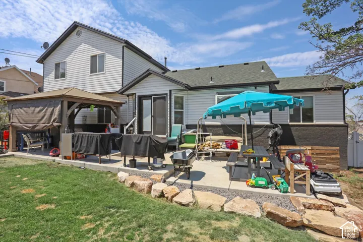 Expansive backyard featuring a concrete patio, built-in gazebo, and terraced landscaping with natural stone elements