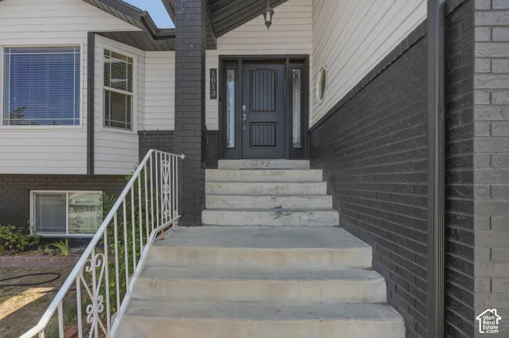 Front entry featuring a dark wood-finish door with decorative glass inserts, concrete steps with a white metal railing, and a combination of white siding and dark brick exterior
