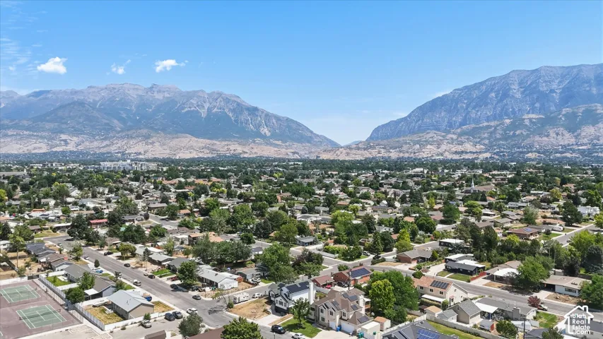 Expansive residential area with a prominent mountain backdrop, featuring numerous mature trees and a clear blue sky