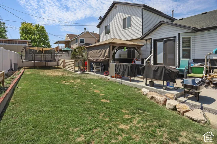 Expansive lawn area with a concrete patio, a built-in gazebo structure, and white vinyl perimeter fencing