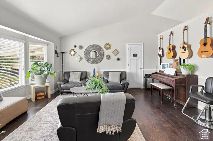 Vaulted ceiling with crown molding, dark wood-finish flooring, white panel door, and bay windows