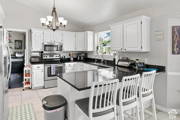 Kitchen featuring white cabinetry, dark countertops, stainless steel appliances, a center island with seating, and tile flooring