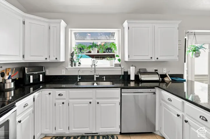 U-shaped kitchen featuring white cabinetry, dark countertops, a stainless steel sink with a gooseneck faucet, and a stainless steel dishwasher