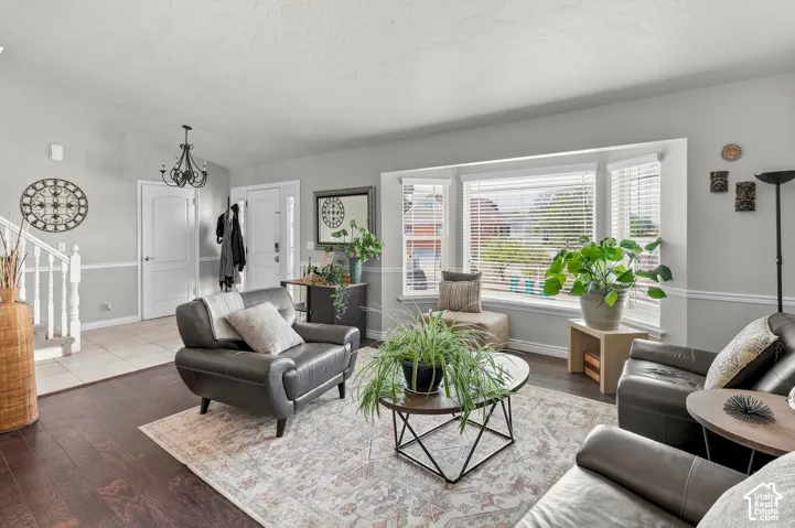 Expansive bay window, wood-finish flooring, staircase with white railing, chandelier, and a front entry door with side window