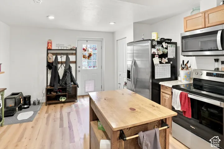 Kitchen featuring wood-finish flooring, stainless steel appliances, upper and lower cabinetry, and a central island with a wood-finish countertop