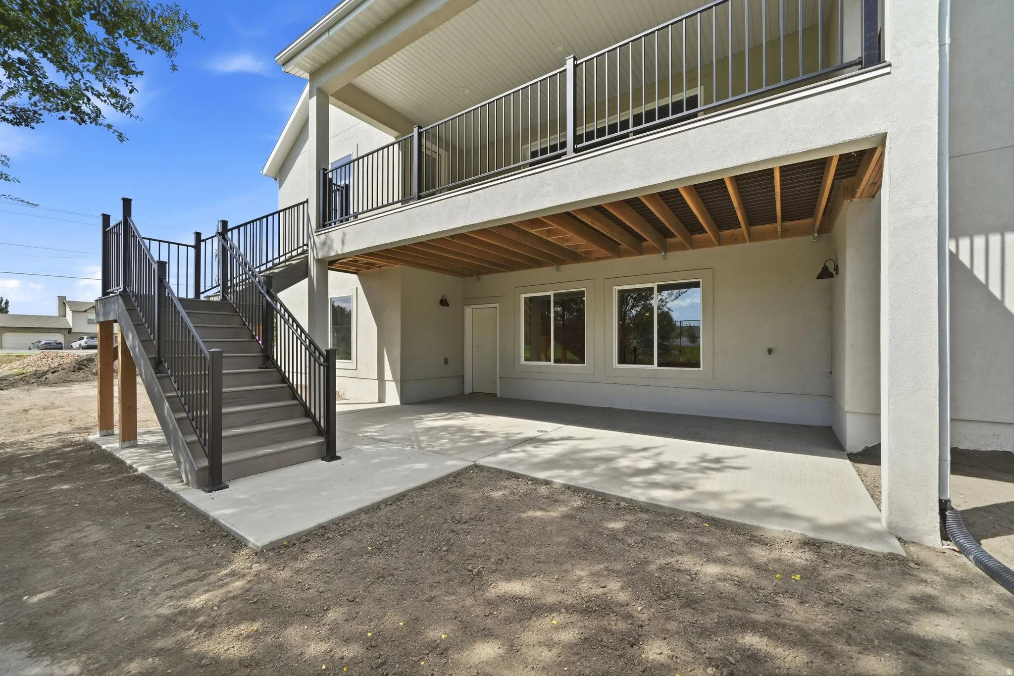 Lower-level patio with concrete surfacing, dual exterior lighting fixtures, and direct access to upper-level decking via stairs with metal railings