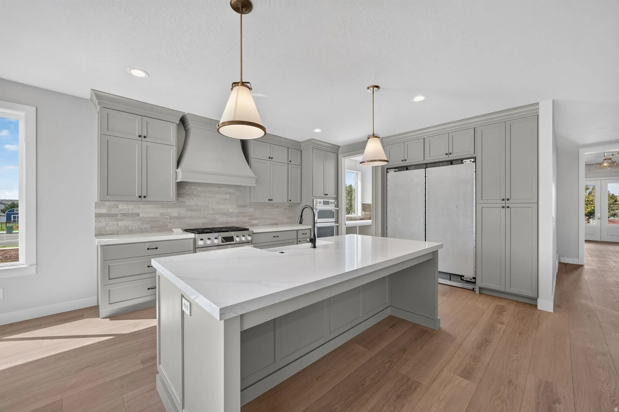 Kitchen featuring abundant grey cabinetry, a central island with a white countertop, wood-finish flooring, a tile backsplash, and stainless steel appliances