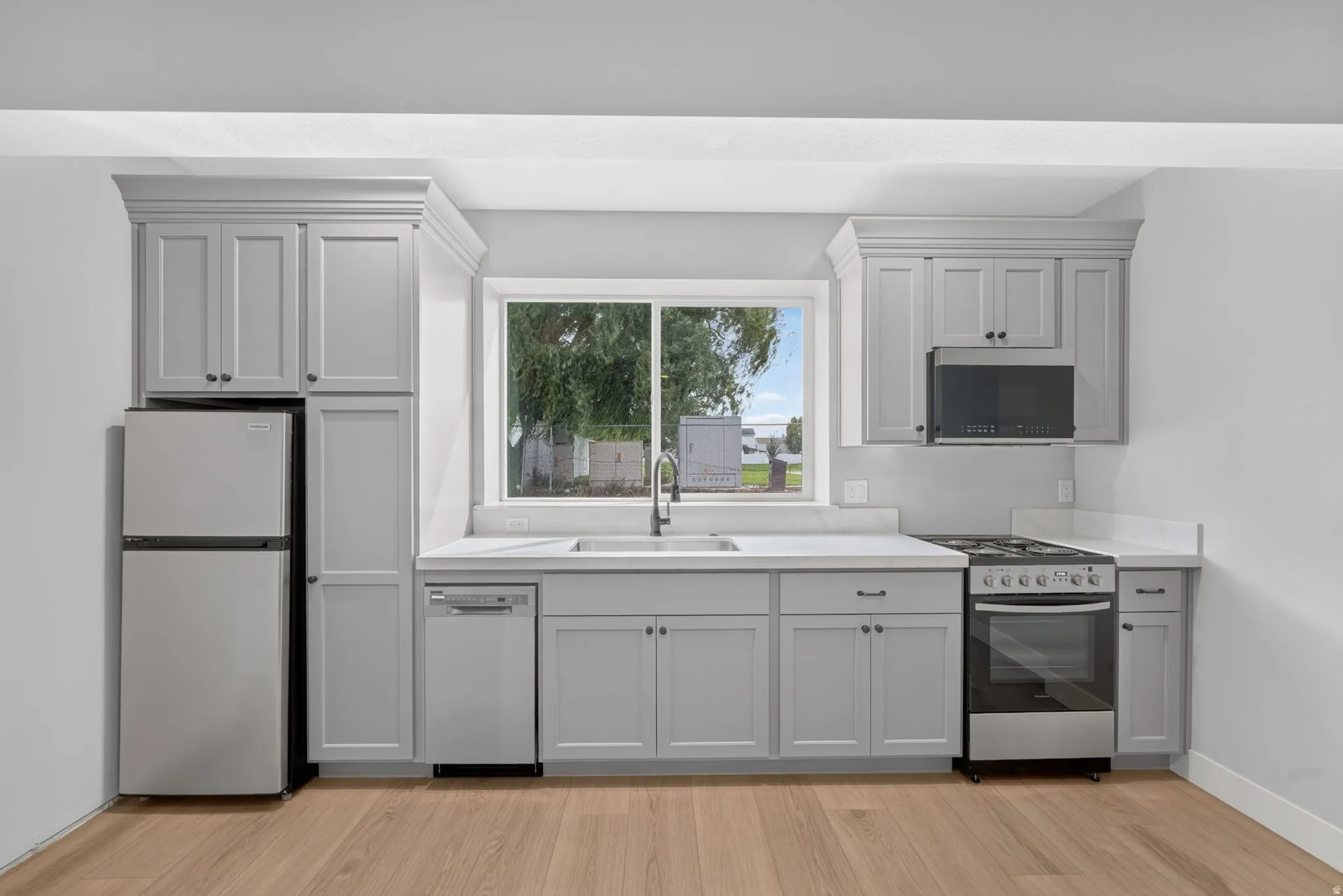Kitchen featuring light wood-finish flooring, light gray cabinetry, white countertops, and stainless steel appliances including a refrigerator, dishwasher, and range