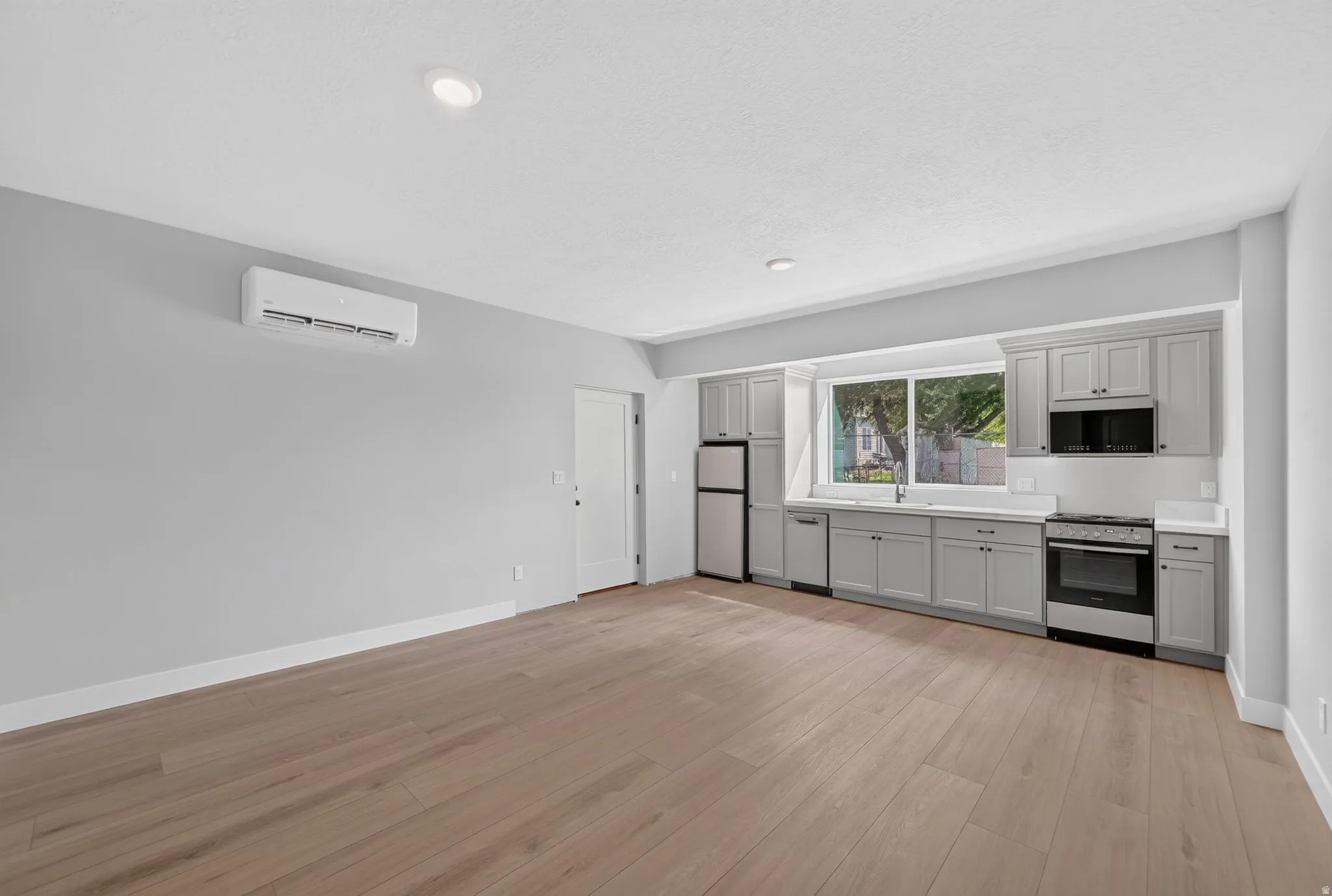 Open-concept kitchen with light gray cabinetry, stainless steel appliances, and wood-finish flooring
