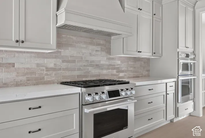 Custom kitchen featuring Shaker-style cabinetry, quartz countertops, a brick-tile backsplash, stainless steel gas range with matching oven, and integrated stainless steel double wall ovens