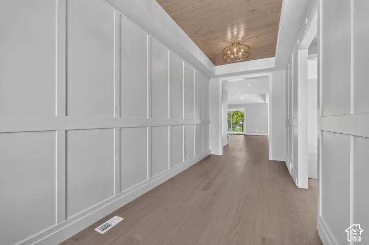 Hallway featuring white board-and-batten wall detailing, wood-finish flooring, a coffered ceiling with light-toned wood plank paneling, and an orbital pendant light fixture
