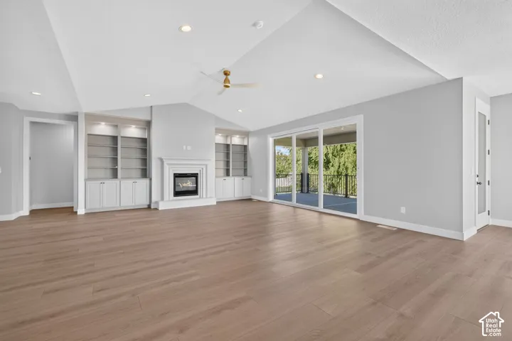 Vaulted ceilings, wood-finish flooring, built-in cabinetry flanking a fireplace, and a large sliding glass door