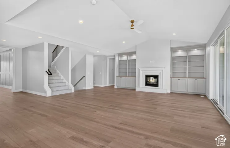 Open floor plan featuring wood-finish flooring, vaulted ceilings with recessed lighting, a fireplace with a mantel, built-in shelving, and sliding glass doors