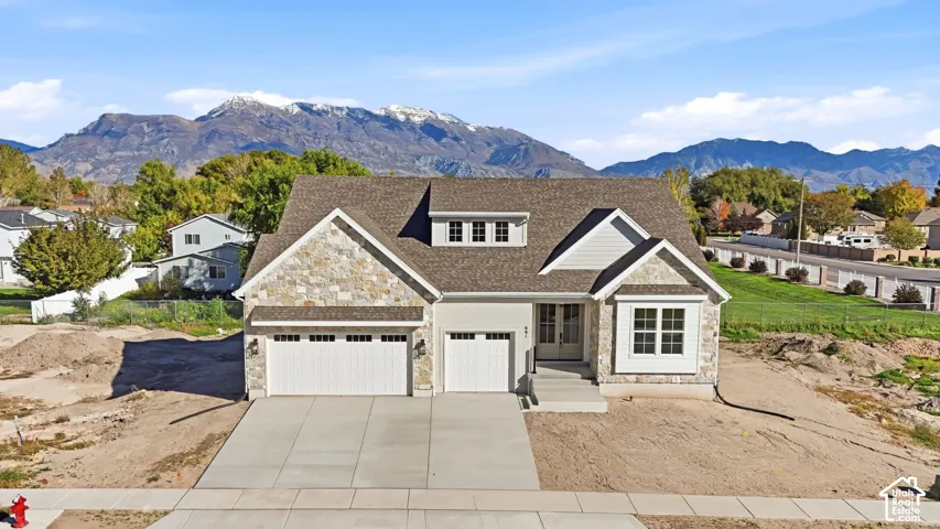 Two-story exterior featuring a stone and siding facade, a three-car garage, a concrete driveway, and a mountain backdrop