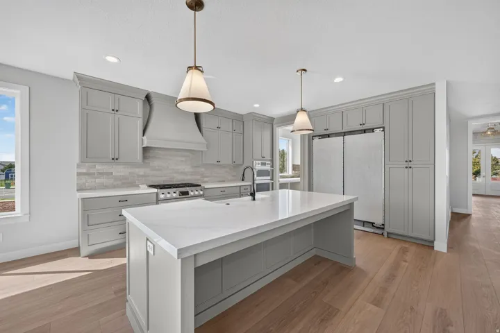 Kitchen featuring abundant grey cabinetry, a central island with a white countertop, wood-finish flooring, a tile backsplash, and stainless steel appliances