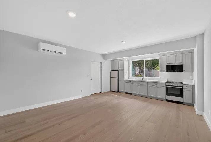 Open-concept kitchen with light gray cabinetry, stainless steel appliances, and wood-finish flooring